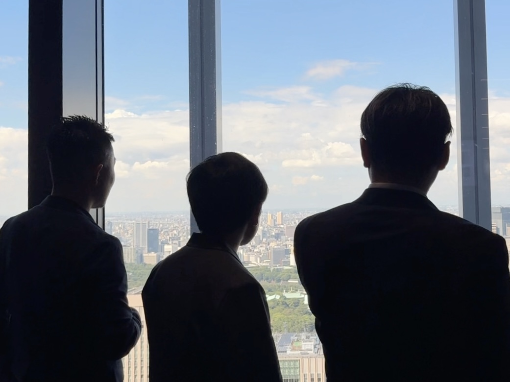 45階の窓辺に立ち、東京の街を見つめる3人の後ろ姿